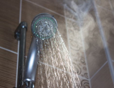 Cabezal de ducha con agua hirviendo y vapor en el baño photo