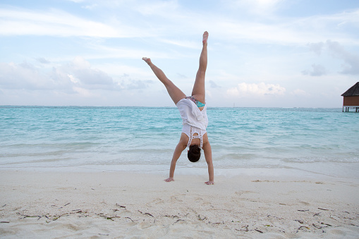This is a beautiful woman jumping around  at a beach at a maldivian island.