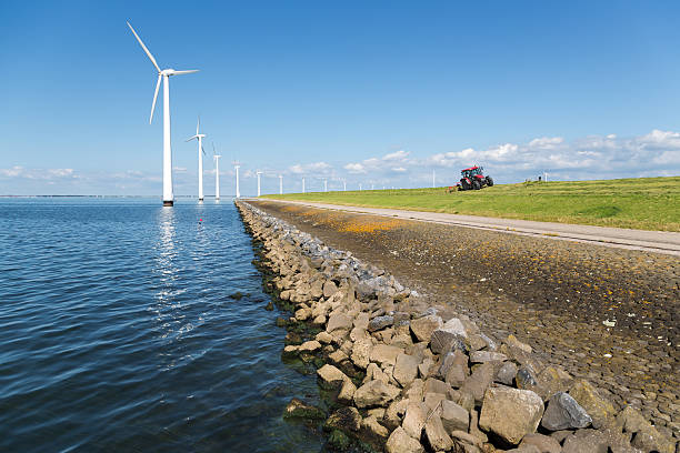 Long row off shore wind turbines in the Dutch sea Long row off shore wind turbines along the Dutch coast with a tractor mowing the grass of the dike dutch culture photos stock pictures, royalty-free photos & images