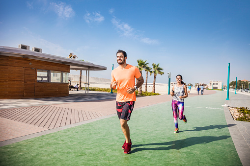 Young athletic couple exercising in Jumeirah Beach promenade in Dubai, UAE. The two guys starting a fitness run on the sidewalk. The sun shines bright on the background.