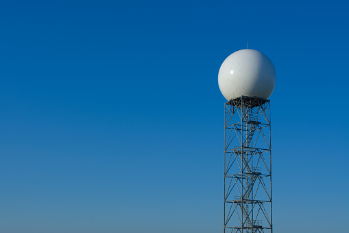 A Doppler Radar tower for weather forcasting with a blue sky background.