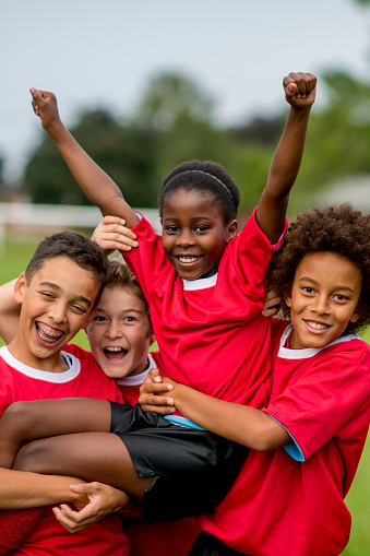 A multi-ethnic group of children enjoying a victory celebration after winning their soccer game, outside at a park - smiling and looking at the camera.