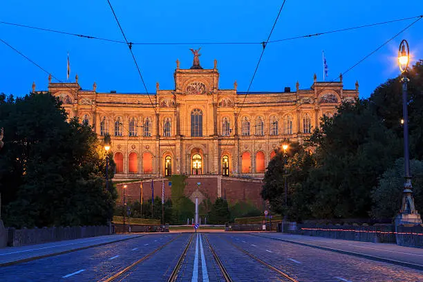 The building called "Maximilianeum" is the seat of the Bavarian State Parliament. This image taken in the blue hour shortly before darkness from the Maximilian Bridge with tramway tracks and overhead contact wires for the tramways.