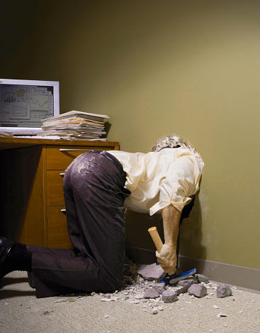 Businessman with his head through a wall in his office.