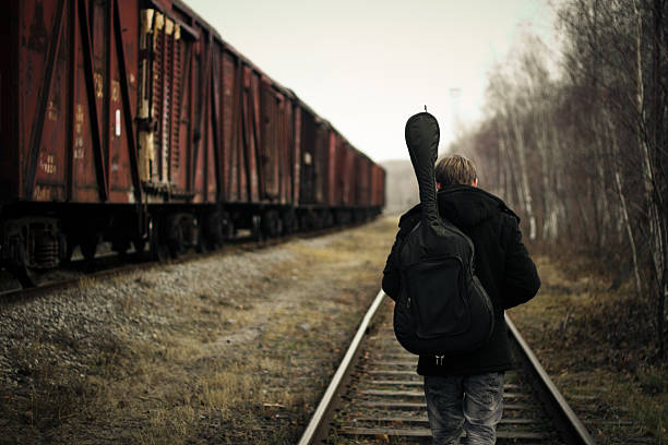 Young guitarist goes along the train on rails in overcast weather.