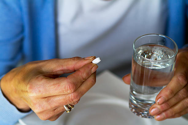 Caucasian senior woman taking cardiac pill A caucasian senior woman is taking pill and is holding a glass with water. Pill is heart illness, cardiac and blood pressure. blood pressure medication stock pictures, royalty-free photos & images
