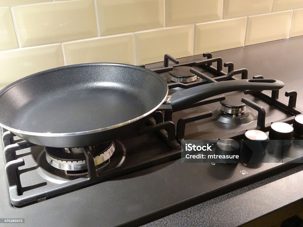 Image of non-stick frying pan, kitchen gas cooker hob rings Photo showing a black, aluminium non-stick frying pan, which is sitting on top of an integrated gas cooker hob, on a granite worktop / countertop.  The gas rings are switched off, after being cleaned. 2015 Stock Photo