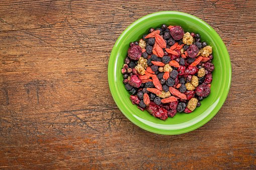 superfruit berry mix (blueberry, mulberry, cherry, goji, elderberry, chokeberry, and cranberry) - green ceramic bowl against grunge wood