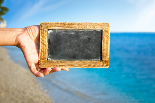 Female hand holding empty blackboard over beautiful sea shore