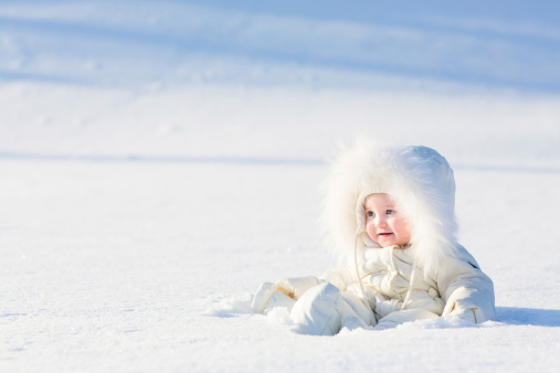 Beautiful baby in white suit sitting at snow field