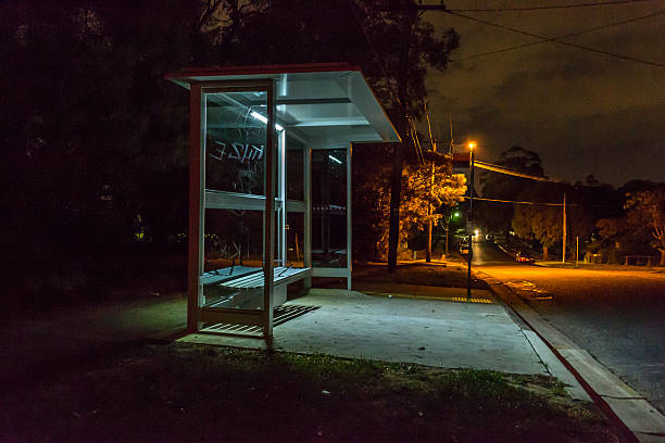 bus shelter at night Empty bus shelter at night. Cars are parked down the road. graffiti is scratched into the glass. bus shelter stock pictures, royalty-free photos & images