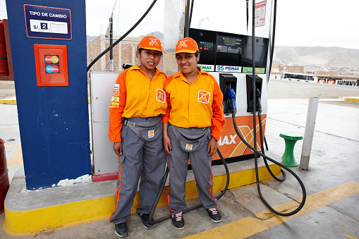 Pucusana, Peru - January 20, 2015: Two peruvian young adult gas station attendants in their distinctive orange and yellow uniforms standing in front of the pumps