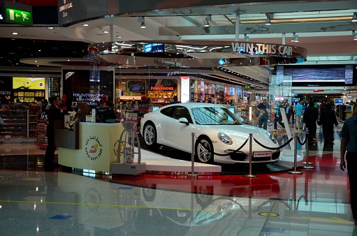 Dubai, United Arab Emirates - March 14, 2015: A Porsche luxury car on display at Dubai airport Duty Free complex. The vehicle is given away to the winner of a raffle. In the background are the duty retail outlets which are popular with travelers at the airport. Dubai airport, homes of Emirates Airline, is one of the busiest airports in the world, well known for its shopping and other facilities. 