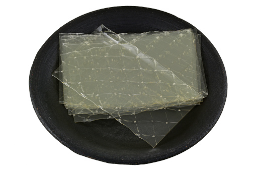 Sheets of Gelatin leaves on a dark ceramic plate, isolated on white