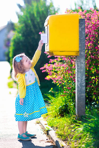 istock Little girl with an envelope next to a mail box 474320420