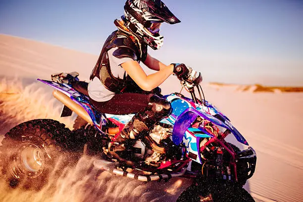 Girl quad bike racer wearing protective gear while racing over sand dunes