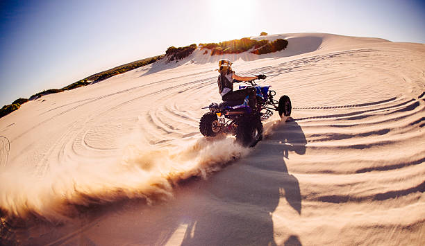 Professional quad biker kicking up sand on a dune Wide angle view of a professional quad biker racing around a sand dune and kicking up a lot of sand quadbike photos stock pictures, royalty-free photos & images