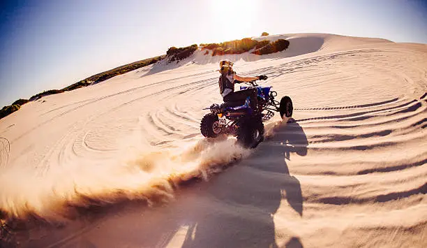 Wide angle view of a professional quad biker racing around a sand dune and kicking up a lot of sand