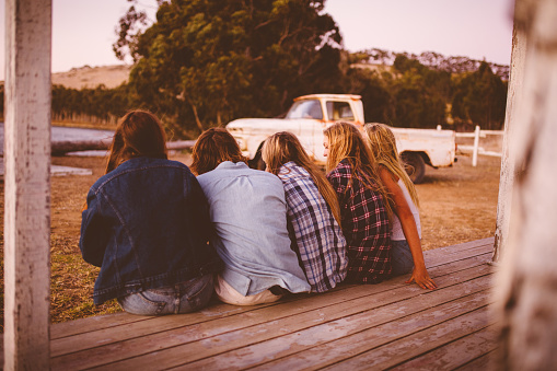 Rearview of a group of teen friends sitting on a porch talking at the end of a day