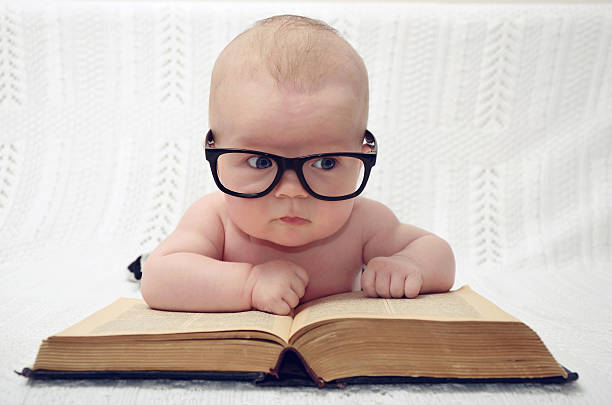 funny portrait of adorable little baby in glasses with old book (thinking expression)