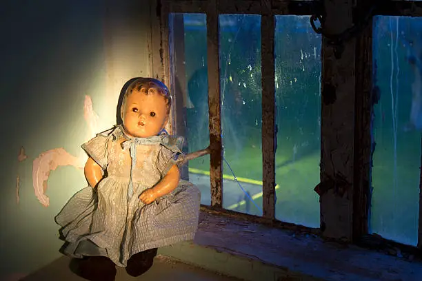 Babydoll in state of deterioration sitting in decaying building window.