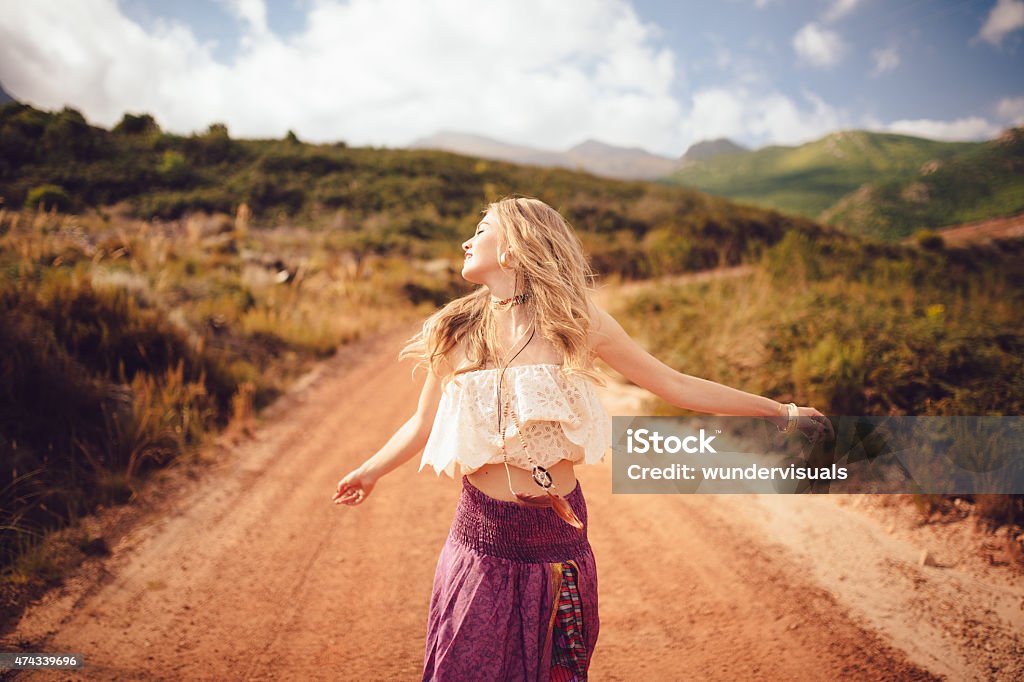 Boho girl on a country dirt road being joyful Boho girl dancing joyfully on a country dirt road in a summer landscape Boho Stock Photo