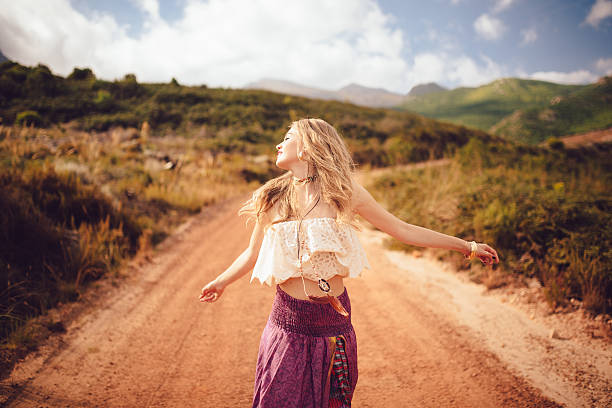 Boho girl on a country dirt road being joyful Boho girl dancing joyfully on a country dirt road in a summer landscape bohemian fashion stock pictures, royalty-free photos & images
