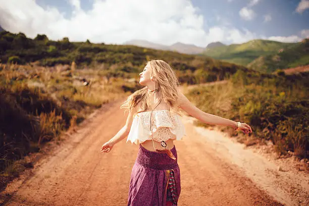 Boho girl dancing joyfully on a country dirt road in a summer landscape