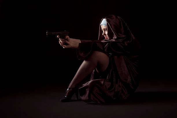 Young nun shoting from gun Nun shooting from gun sitting on her knees. Low key photo on black background. nun catholicism sister praying stock pictures, royalty-free photos & images