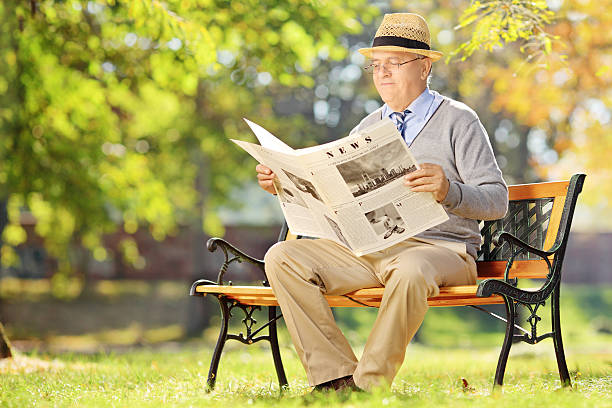 istock Senior gentleman with hat sitting on bench and reading newspaper 474344159
