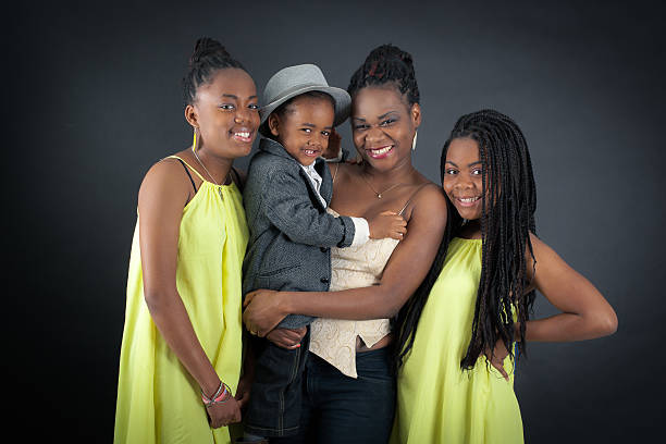 Portrait of middle aged Black woman standing between young multiethnic woman and man smiling with eyes closed in photo booth, all embracing closely in front of curtain