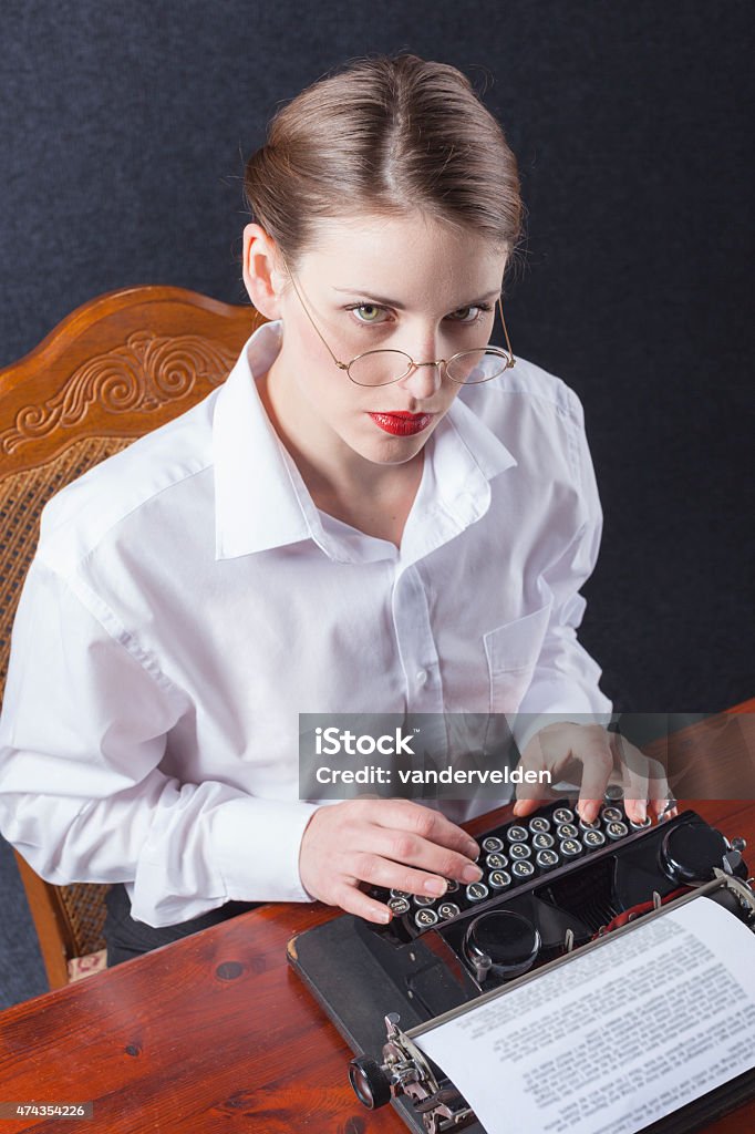 Severe Secretary From The 1930s Or 1940s A rather smart secretary or typist from the 1930s era looking up during typing a very important letter. Her typewriter and spectacles are period items. 1930-1939 Stock Photo