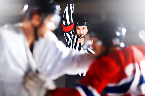 Two male ice hockey players in a fight during game. They grabbed each other and throwing punches. Referee is trying to stop them. Wearing white and red jerseys. Common scene in hockey game.
