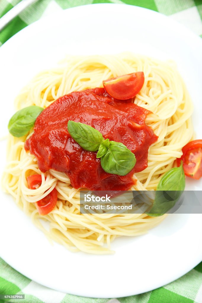 Spaghetti with tomatoes and basil on plate Spaghetti with tomatoes and basil on plate on white wooden background 2015 Stock Photo