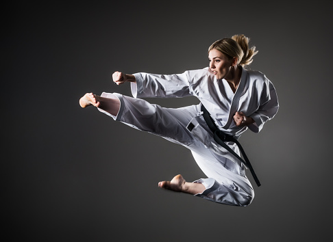 Girl performs a kick in jump at dark gray background, 