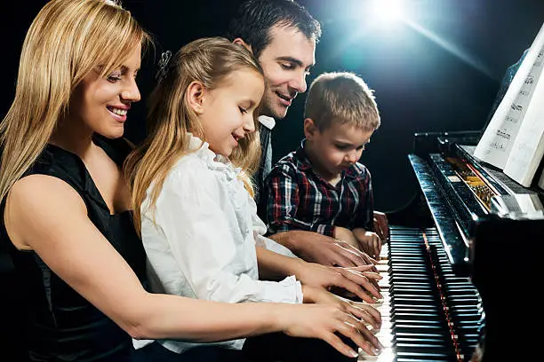 Mid adult parents teaching their children how to play piano.