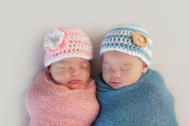 Fraternal Twin Baby Brother and Sister Five week old sleeping boy and girl fraternal twin newborn babies. They are wearing crocheted pink and blue striped hats. cap hat photos stock pictures, royalty-free photos & images