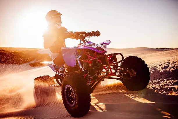 Competitive quad biker with bright sun flare behind driving in a desert race