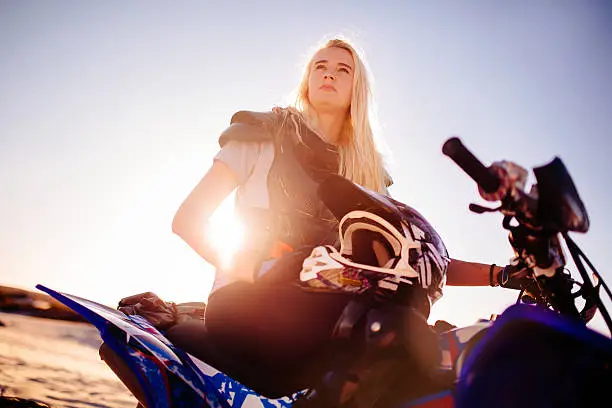 Female quad bike racer looking intently into the distance thinking about her competition with sun flare behind her