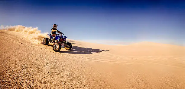 Professional quad biker racing downhill over a sand dune in a desert race