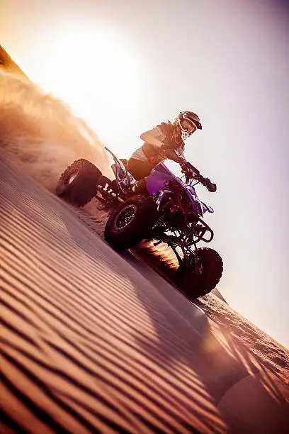 Pro quad biker driving on a sand dune while involved in a desert race