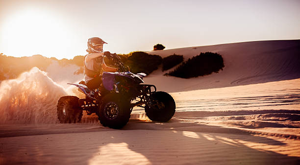 Quad bike racer in protective gear driving on sand dunes stock photo