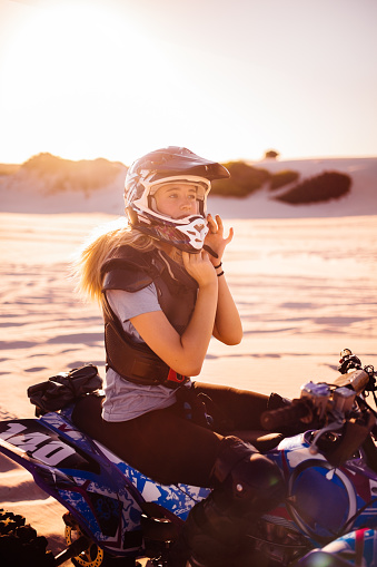 Professional young female quad bike racer sitting on her four-wheeler in sand dunes