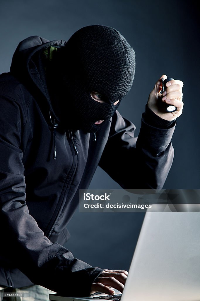 Identity thief A masked intruder hacking into a laptop computer. Adult Stock Photo