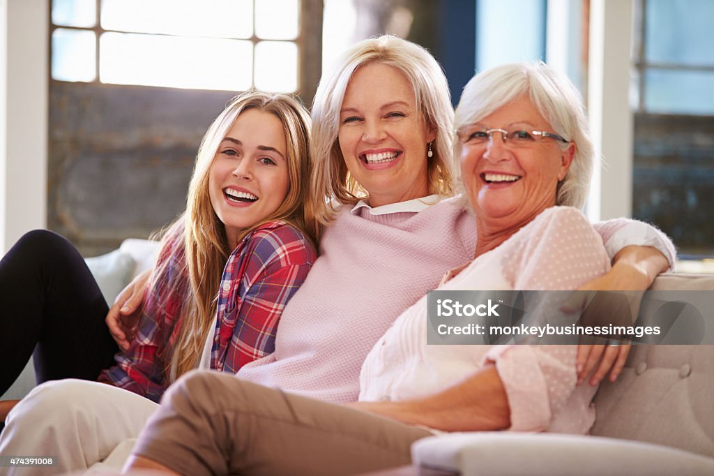 Grandmother With Mother And Adult Daughter Relaxing On Sofa Grandmother With Mother And Adult Daughter Relaxing On Sofa, Smiling To Camera Multi-Generation Family Stock Photo