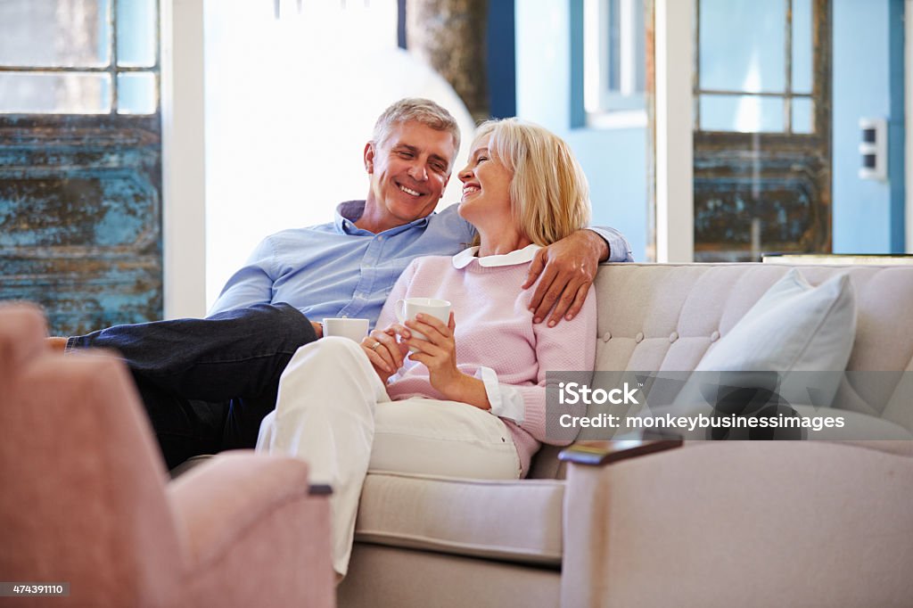 Mature Couple At Home Relaxing In Lounge With Hot Drink Mature Couple Stock Photo