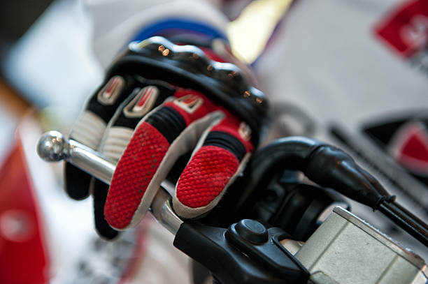 Serious motorcyclist in helmet putting gloves on hands while preparing for riding outdoors, lens flare effect