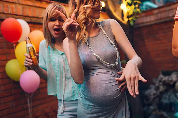 Beautiful young lesbian couple dancing together at backyard party. Lesbian couple expecting baby. Selective focus to pregnant woman.