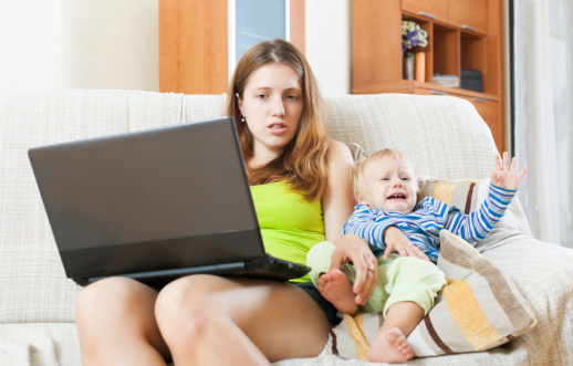 Whiner woman with a crying baby, working with a computer at home