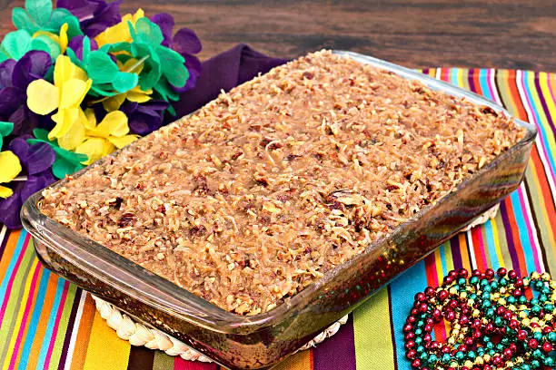 Full sheetcake of a cajun cake with praline topping in a mardi gras setting.